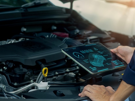 Mécanicien utilisant une tablette avec schéma holographique bleu d'un moteur pour diagnostic automobile sous le capot.