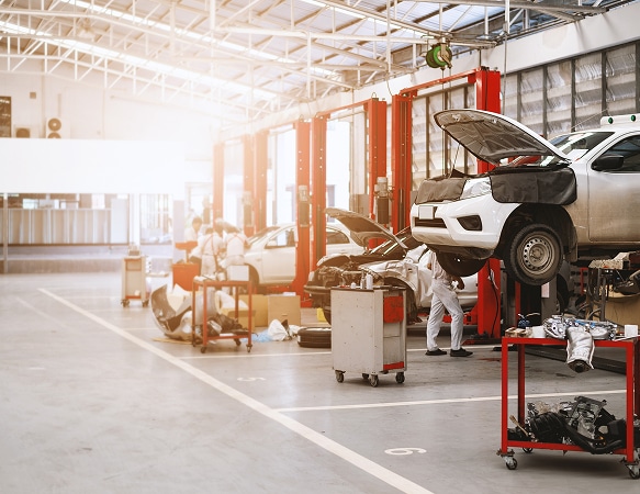 Réparation automobile : Atelier moderne avec véhicules sur ponts Garage automobile moderne et lumineux avec mécaniciens en blouse blanche réparant des véhicules sur des ponts élévateurs rouges, moteur apparent.