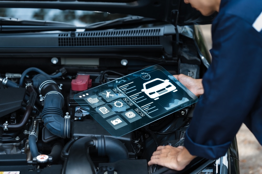 Diagnostic auto : la technologie au service du mécanicien. Technicien utilisant une tablette transparente pour diagnostic automobile high-tech. L'écran affiche l'état du moteur (52%) et des icônes de maintenance.