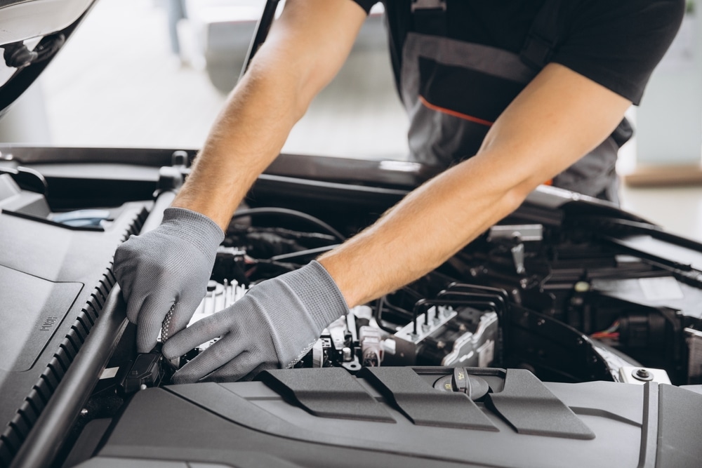 Mécanicien expert inspectant et réparant le moteur. Mécancien en gants gris manipule les composants du moteur sous le capot ouvert du véhicule. Inspection ou réparation dans un garage. Texte "PUSH" visible.